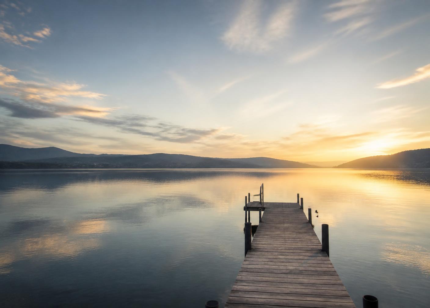 A quiet wooden dock reaching into still harbor water at dawn